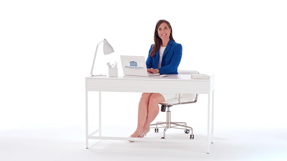 A woman in blue sits at a desk in white space, surrounded by white props.