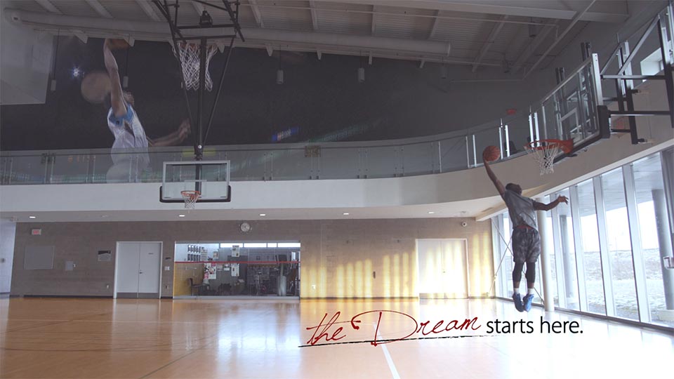 A young YMCA basketball player slam dunks with the text "The dream starts here".