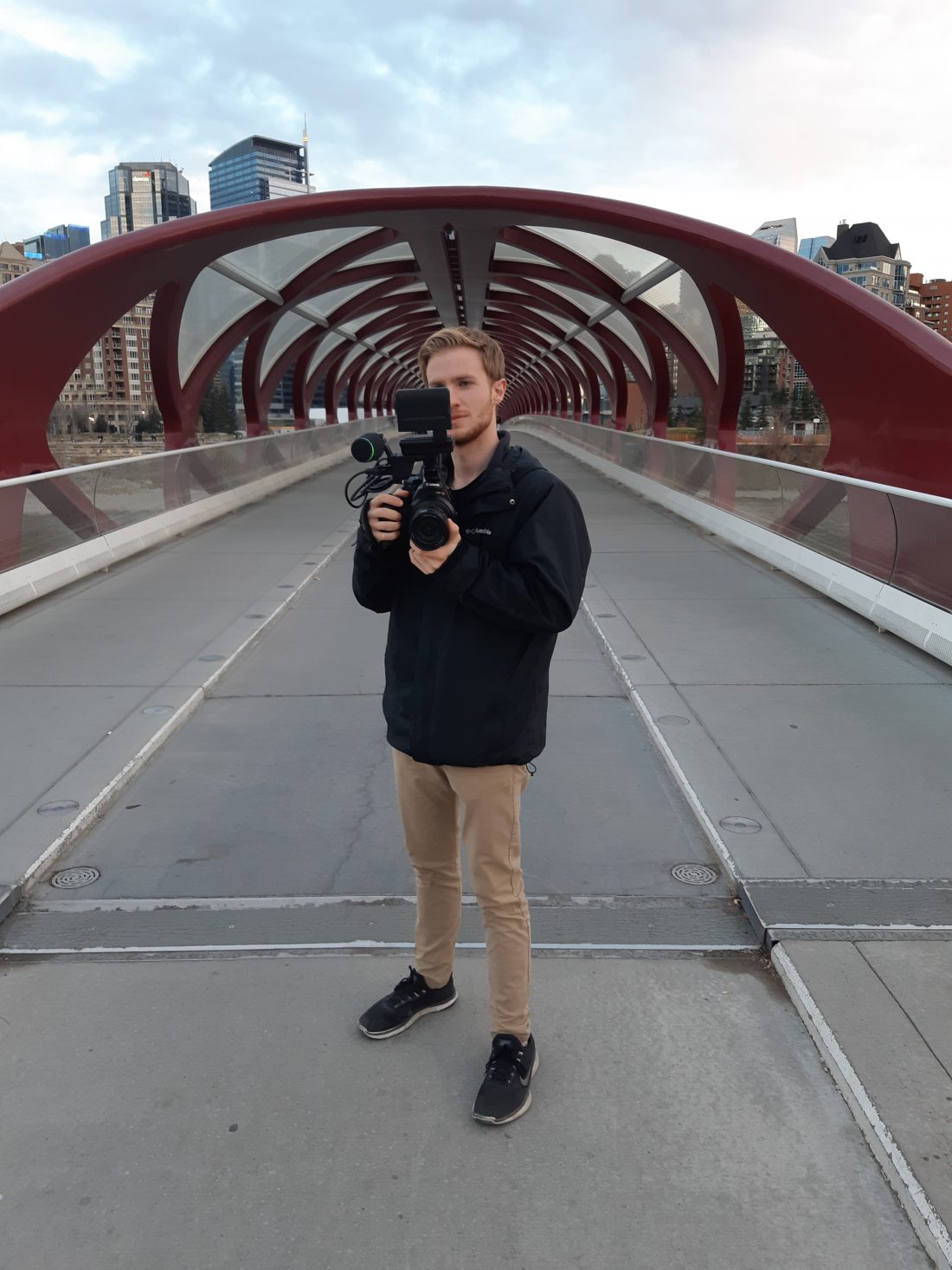 Sam stands in the middle of a bridge filming